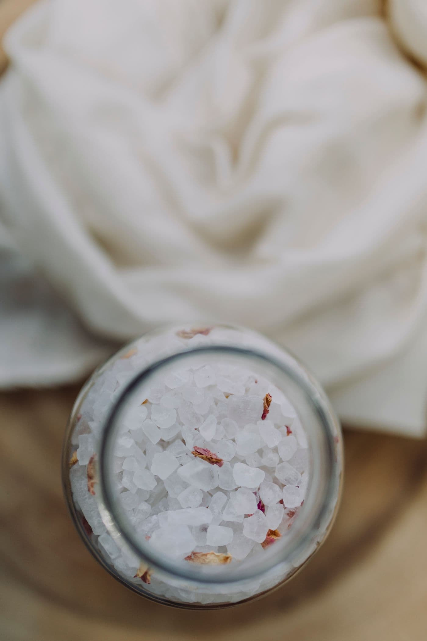 Jar of Clay Soak Bath Salts filled with mineral salts, set against soft draped fabric.