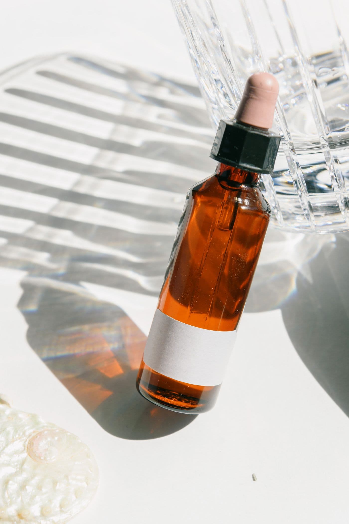 Amber dropper-style bottle of Ember Clay Eau de Parfum beside a seashell, cast in dramatic shadow.