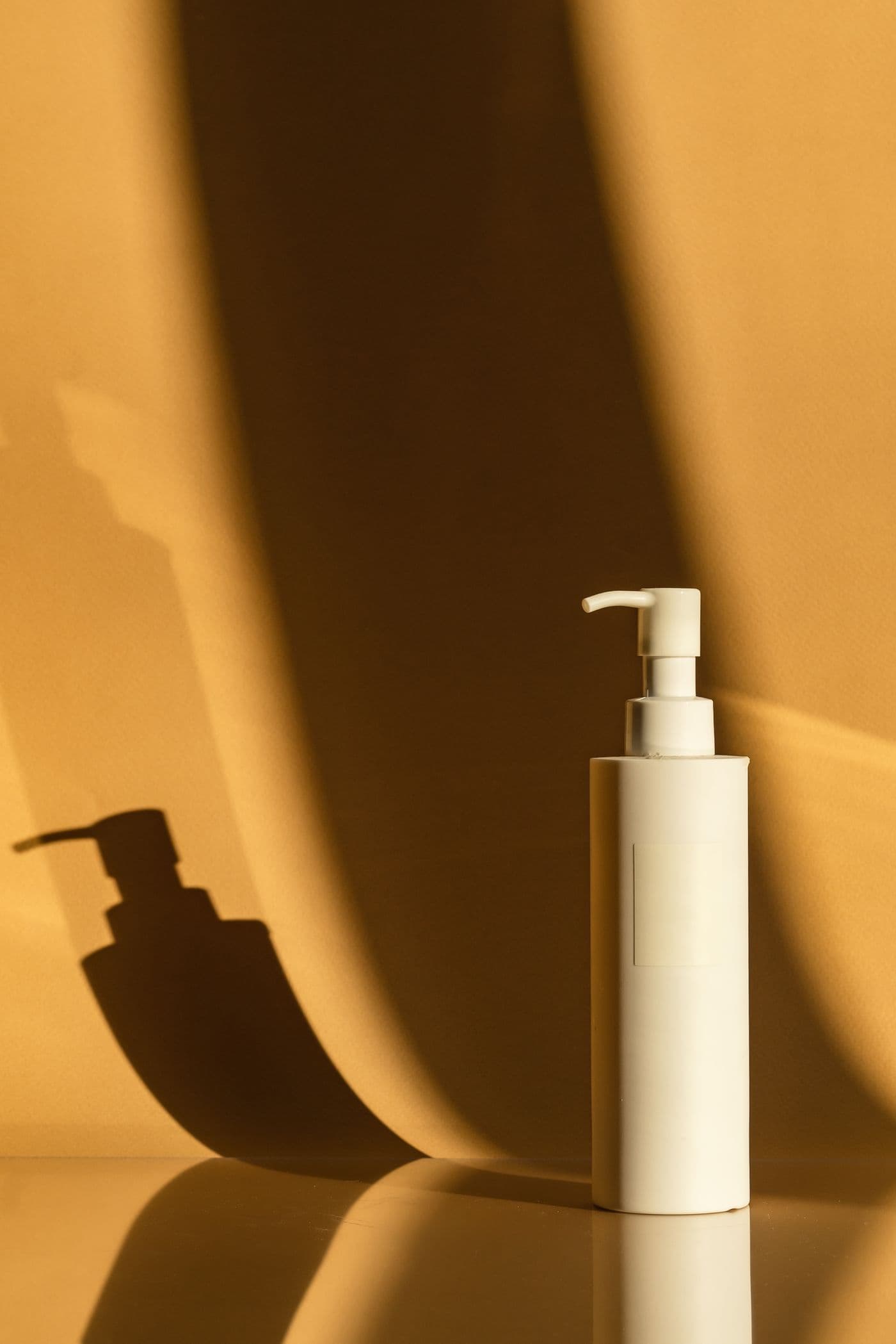 White pump bottle of Moss Milk Body Wash standing against a warm mustard-toned background with a long shadow.