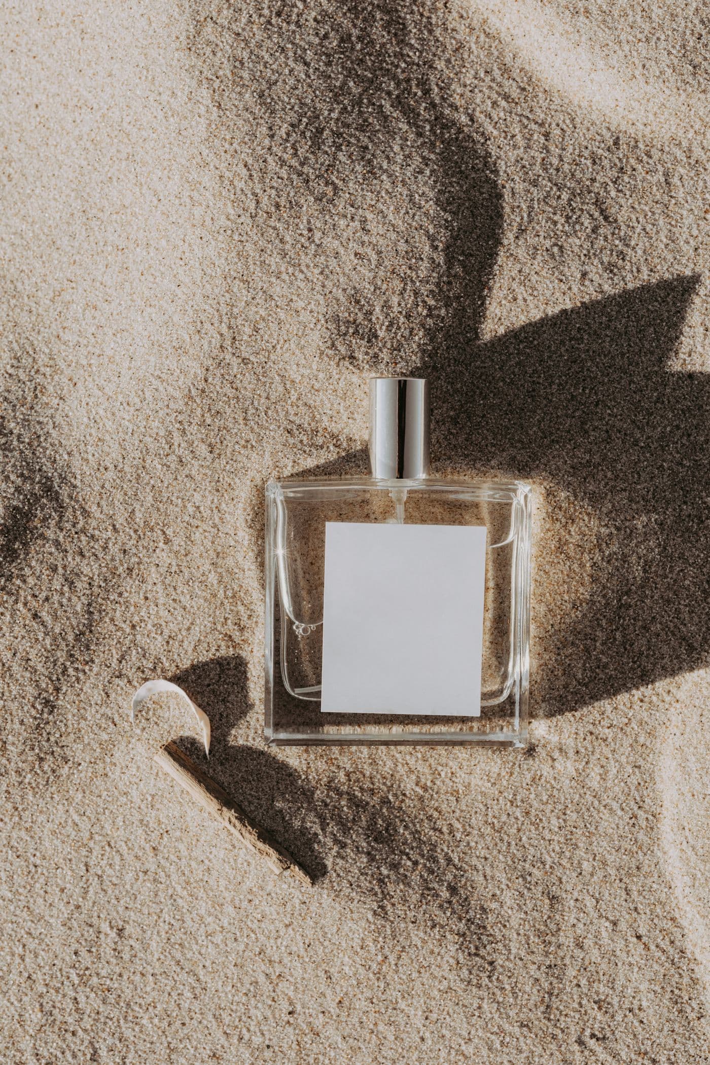 Rectangular glass bottle of Sauge Eau de Parfum resting in sand with soft natural light.