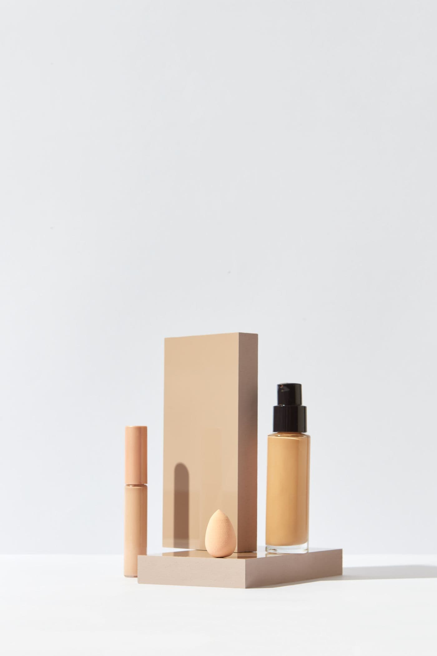 Silk Veil Foundation bottle displayed on a geometric plinth alongside a concealer stick and makeup sponge.